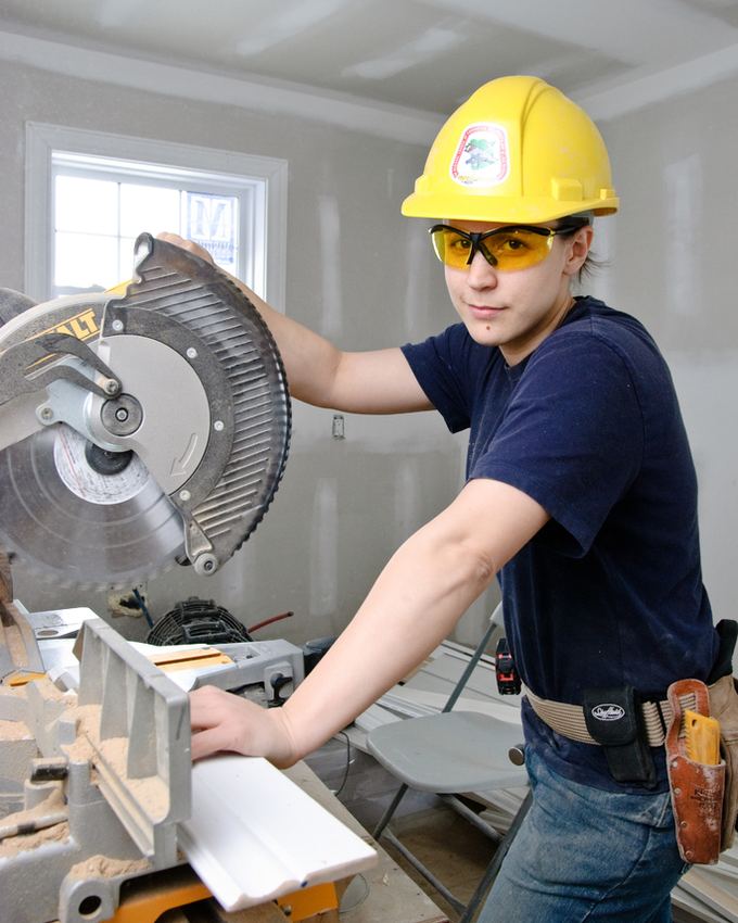 A carpenter in a hard hat and safety glasses using a mitre saw