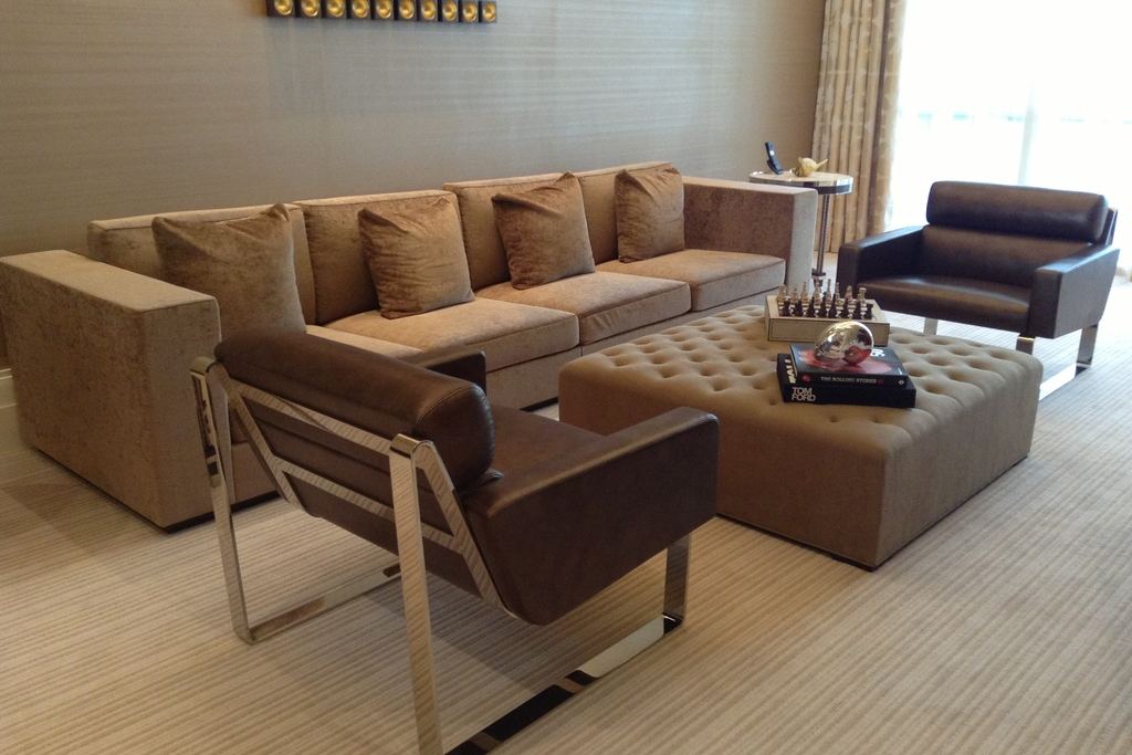 A calm living room with a deep sofa, an upholstered ottoman and soft window light