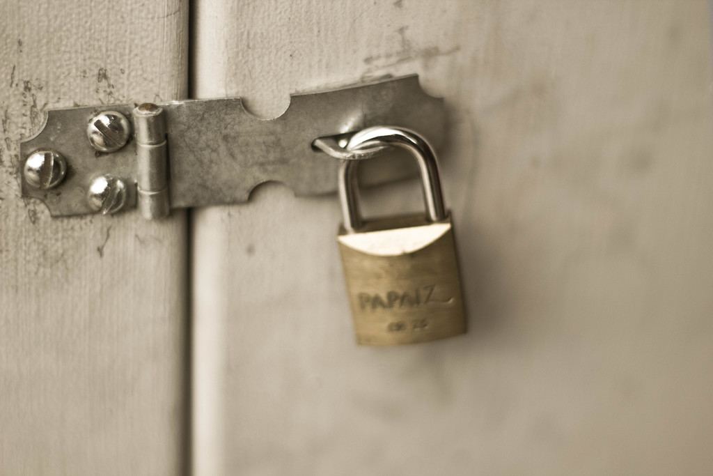 A brass padlock fastened through a hasp on a painted door